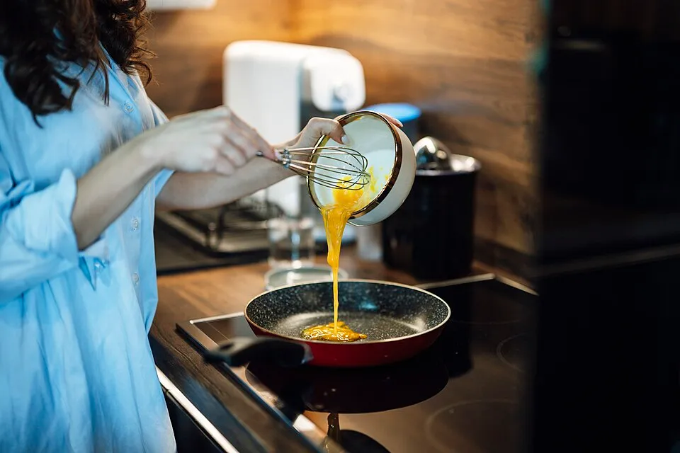 Woman pouring whisked eggs into a frying pan for a protein-rich breakfast