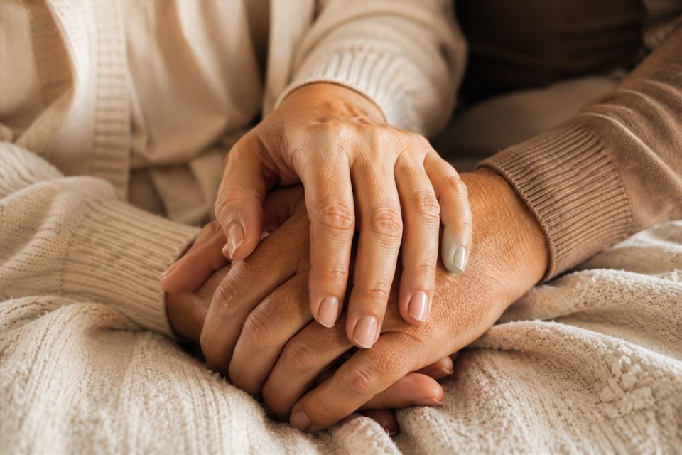 Close-up of two hands gently intertwined, resting on a soft blanket