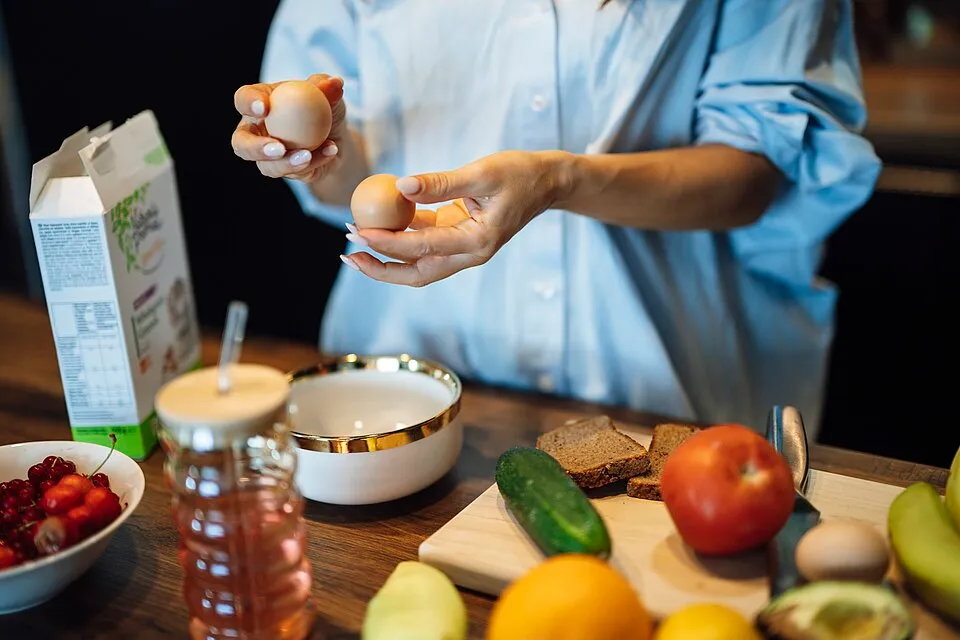 Hands holding fresh eggs over a kitchen table with fruits, vegetables and whole-grain bread