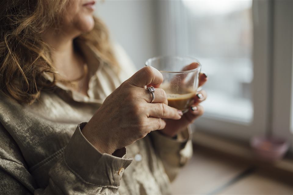 Close-up of a woman's hands holding a warm drink by a window