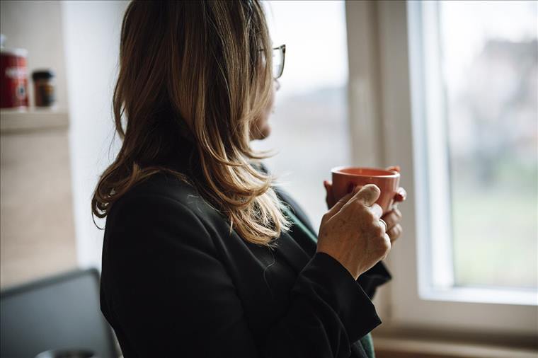 Woman with a cup of coffee looking out her kitchen window