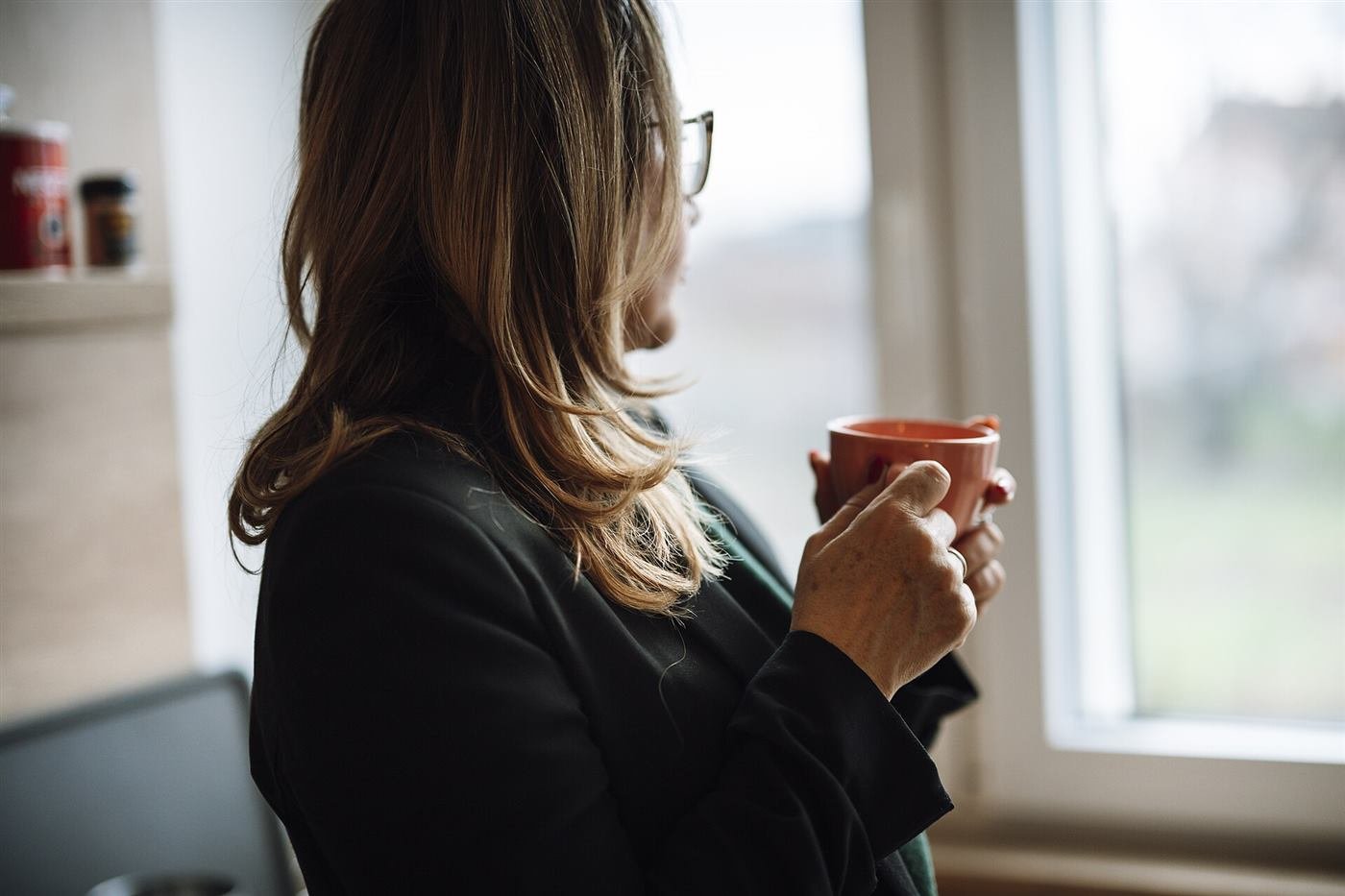 Woman with a cup of coffee looking out her kitchen window