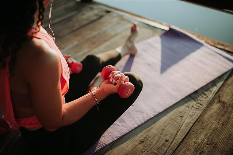 Woman training with dumbbells on a yoga mat outdoors in golden evening light