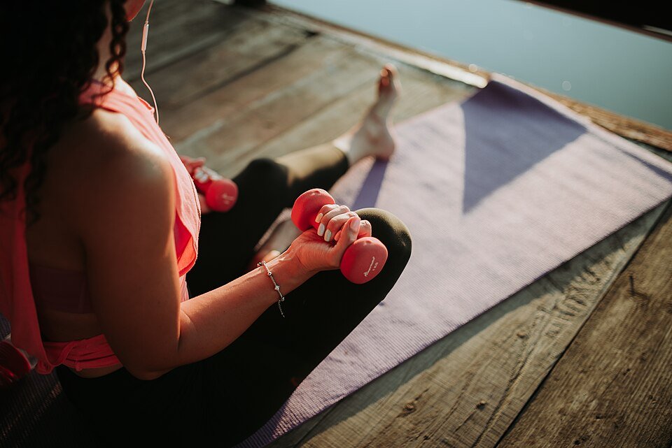Woman training with dumbbells on a yoga mat outdoors in golden evening light