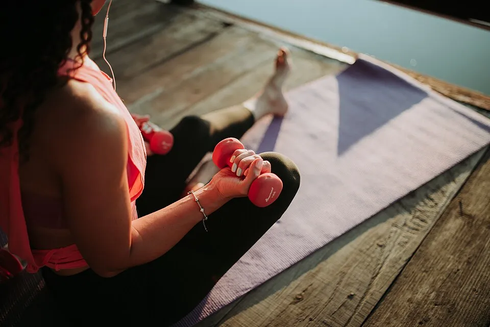 Woman training with dumbbells on a yoga mat outdoors in golden evening light