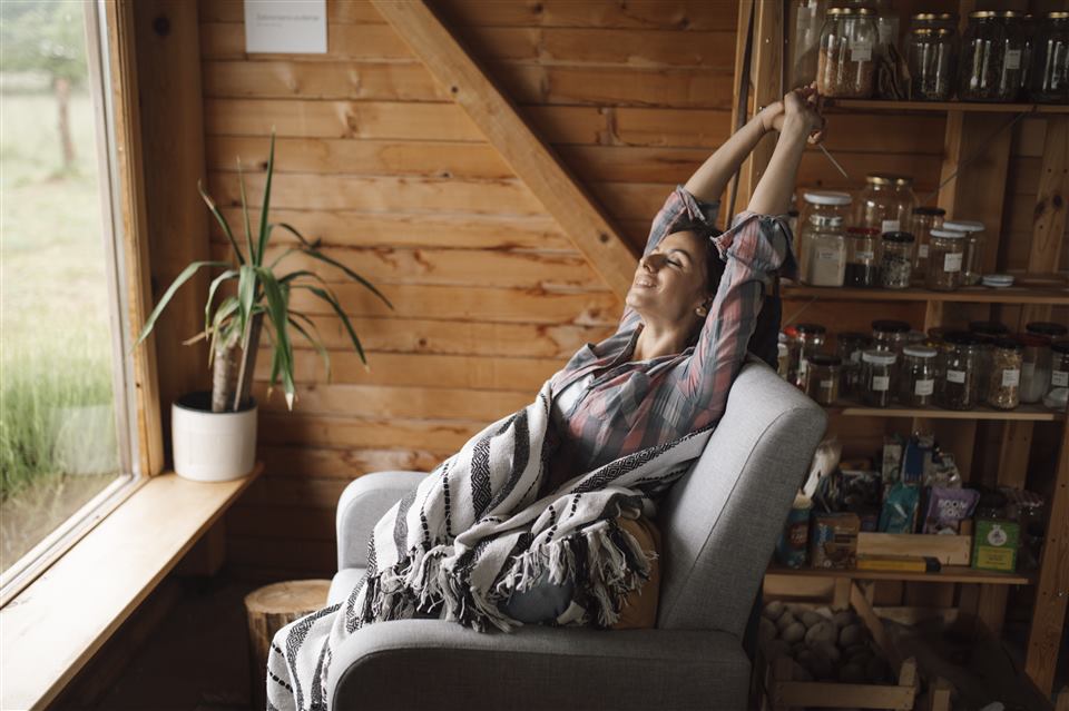 Woman stretching and relaxing in a cozy chair wrapped in a blanket, smiling with eyes closed