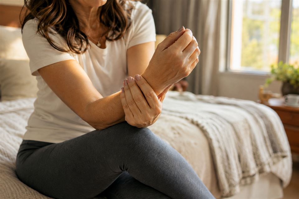 Woman gently holding her own wrist while sitting on the edge of a bed